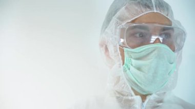 Tanımlanamayan Kafkasyalı sıhhiyeci test yapıyor, kafasını çeviriyor, cam şişeyi kanla inceliyor, yazıyı okuyor. Virolog adam koruyucu giysi giyiyor, lastik eldiven, beyaz duvar arkasında izole edilmiş..