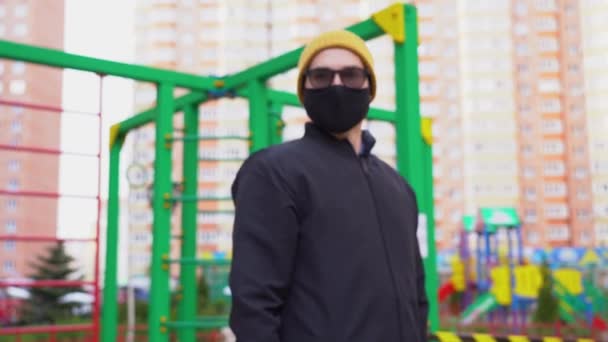 感染者は カラフルな子供の遊び場の背景にジェスチャーを禁止停止させる保護顔マスク 黒いジャケット 青い手袋 眼鏡を着用してください コンセプトをロックダウン — ストック動画