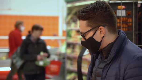 若いブルネットの男の肖像画は 保護顔マスク 黒眼鏡 冬のジャケットを着用してください 男性はスーパーの近くを背景にオレンジのおいしい香りを嗅ぎます 新年の準備 鍵をかけて — ストック動画