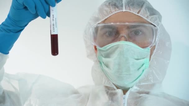 自信を持って科学者男性は 新しい実験ワクチンを使用した後 Covid 19陰性の血液検査管を見て 手で保持保護スーツ 顔マスク ゴム手袋を着用します 人々のための薬を作ったコンセプト — ストック動画