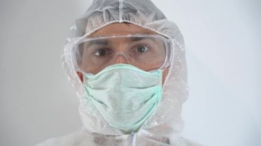 Koruyucu giysi giyen bulaşıcı hastalıklar doktoru, mavi lateks tıbbi eldiven giyen doktor, beyaz duvar hastanesi arka planında Covid-19 'un kırmızı kan testinin negatif işaretli el cam tüpünü elinde tuttuğunu gösteriyor..