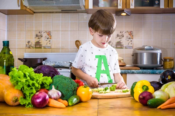 The young boy in cooking standing in the kitchen near table with vegetables. — Stock Image Young Boy Cooking Standing Kitchen Table Vegetables Royalty Free Stock Photos