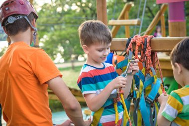 İp parkta katılmak için kask ve emniyet kemerleri koymak için küçük çocuk yardımcı eğitmen. Etkin sağlıklı boş zaman kavramı çocuklu harcama.