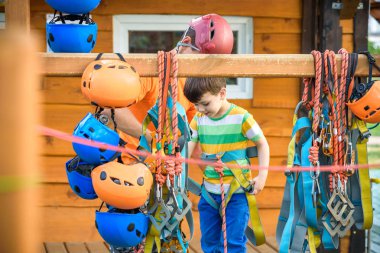 İp parkta katılmak için kask ve emniyet kemerleri koymak için küçük çocuk yardımcı eğitmen. Etkin sağlıklı boş zaman kavramı çocuklu harcama.