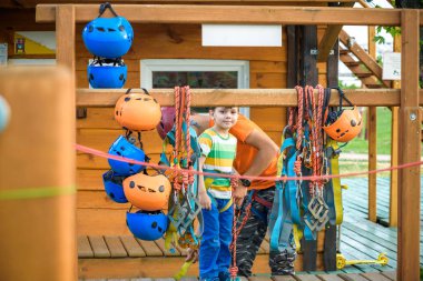 İp parkta katılmak için kask ve emniyet kemerleri koymak için küçük çocuk yardımcı eğitmen. Etkin sağlıklı boş zaman kavramı çocuklu harcama.