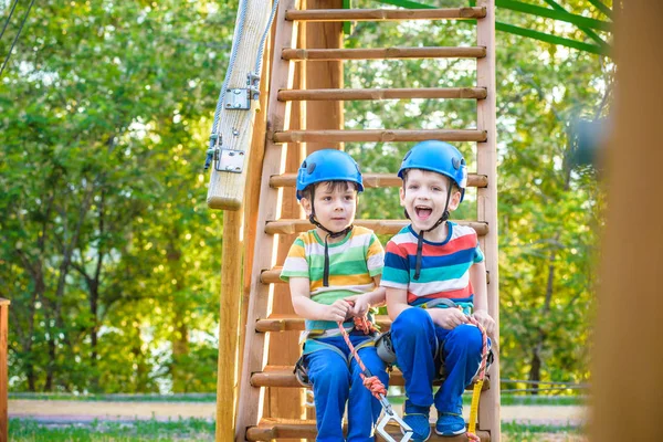 Macera Parkı içinde tırmanma ikiz kardeşler çok çeşitli egzersizler, engel kursları ve ZIP-hatları tırmanma halat gibi öğeleri içerebilen bir yer var. Ahşap merdivenlerde oturan çocuk çocuklar.