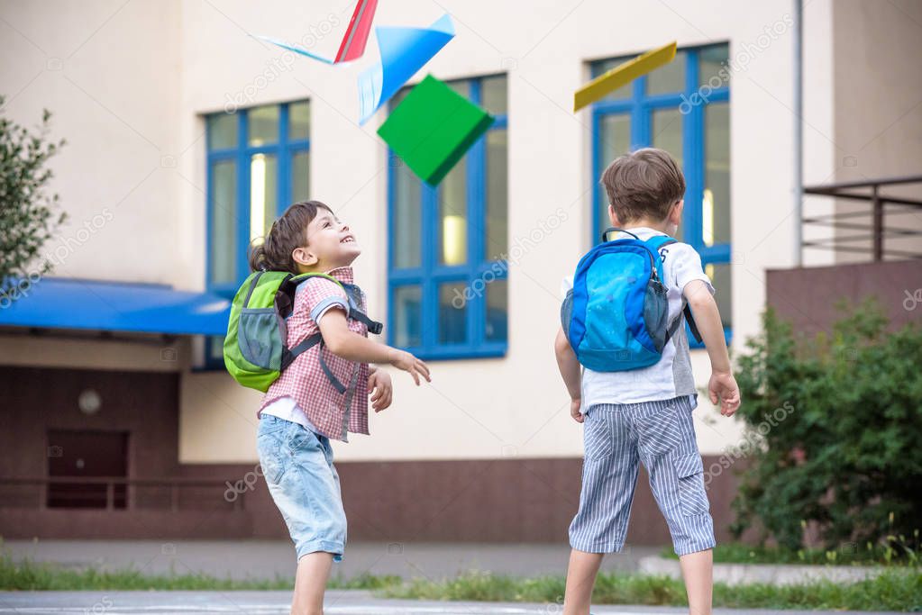 Happy children - two boys friends with books and backpacks on the first or last school day. Schoolchildren celebrating end of term. Students to complete academic year. Full length outdoor portrait.