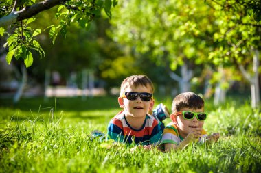 Mutlu gülümseyen erkek kardeş kardeşi çimenlerin üzerinde rahatlatıcı. Kopya alanı görünümüyle kapatın. Okul öncesi çocuklar güneş gözlüğü takıyor yaz tatil kampı. Gevşeme mutlu çocukluk dostluk kavramı.