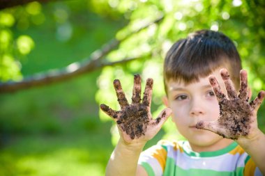 Çamur ve kumsalda oynadıktan sonra kirli ellerini gösteren beyaz bir çocuk. Güneşli bahar ya da yaz akşamları çiçek ağaçlarının arka planında. Mutlu çocukluk arkadaşlığı kavramı.