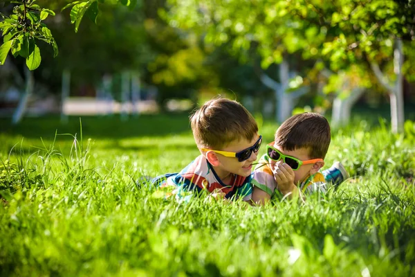 Mutlu gülümseyen erkek kardeş kardeşi çimenlerin üzerinde rahatlatıcı. Kopya alanı görünümüyle kapatın. Okul öncesi çocuklar güneş gözlüğü takıyor yaz tatil kampı. Gevşeme mutlu çocukluk dostluk kavramı.