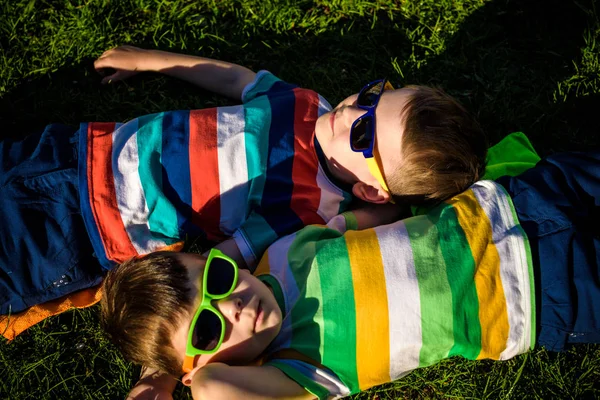 Mutlu gülümseyen çocuklar, çimenlere uzanmış, güneş gözlüğü takmış, kameraya gülümsüyor, yukarıdan çekim yapıyorlar. Mutlu çocukluk arkadaşlığı kavramı.