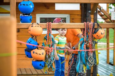 İp parkta katılmak için kask ve emniyet kemerleri koymak için küçük çocuk yardımcı eğitmen. Etkin sağlıklı boş zaman kavramı çocuklu harcama.