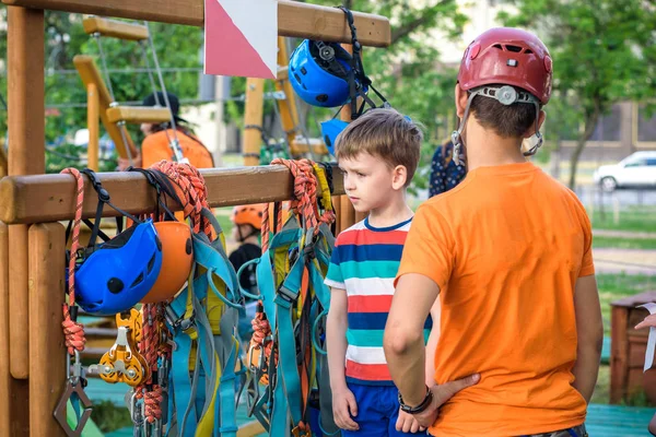 İp parkta katılmak için kask ve emniyet kemerleri koymak için küçük çocuk yardımcı eğitmen. Etkin sağlıklı boş zaman kavramı çocuklu harcama.