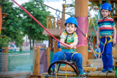 Küçük şirin çocuk aktivite bir tırmanma macera parkta yaz güneşli bir günde zevk. bir ip Bahçesi yapısında tırmanma yürümeye başlayan çocuk. Kask ve kemer ile güvenli tırmanma aşırı spor. sigorta