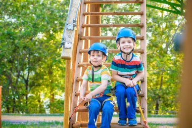 Macera Parkı içinde tırmanma ikiz kardeşler çok çeşitli egzersizler, engel kursları ve ZIP-hatları tırmanma halat gibi öğeleri içerebilen bir yer var. Ahşap merdivenlerde oturan çocuk çocuklar.