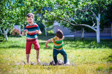 Küçük bir çocuk ve onun kardeşi yaz parkta oynamak. Çocuk renkli giysileri ile su birikintisine atlamak ve bahçede çamur. Çocuklar yaz su birikintisine duştan sonra yürümek. Herhangi bir hava açık eğlence.