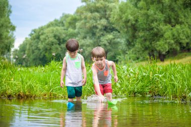 Kağıt tekne bir nehir veya göl ile sıcak ve güneşli yaz gününde oynayan iki küçük kardeş kardeş. Çocuklar için etkin boş. Çocuk çocuk en iyi arkadaşlar açık havada birlikte eğleniyor.