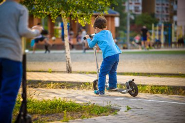 İki sevimli çocuklar, rekabet scooter, park, açık sürme yaz. Çocuklar dışarıda oynarken mutluyuz. Onların scooter üzerinde duran iki kardeş.