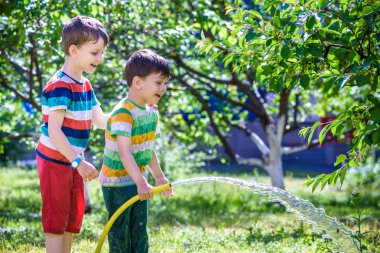 Mutlu çocuk çocuk bir hortum su dökülen. Çocuklar köyü açık havada bahçede meyve sulama ile eğleniyor. Komik tatil eğlence su çocuklar için.