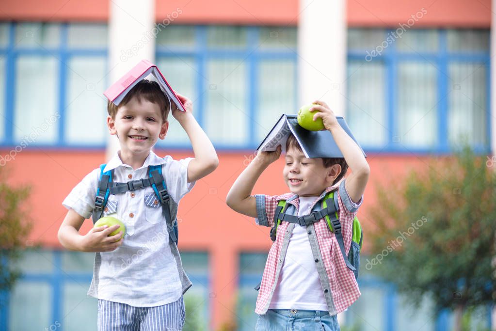 Child going to school. two boy friend holding books on head house roof, first school day. Little students excited to be back to school. Beginning of class vacation. Kids eating apple in yard