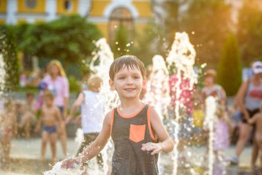 Heyecanlı çocuk su jetleri, Çeşme arasında eğleniyor. Şehirde yaz. Çocuk mutlu gülümseme yüzünü. Ekoloji kavramı.