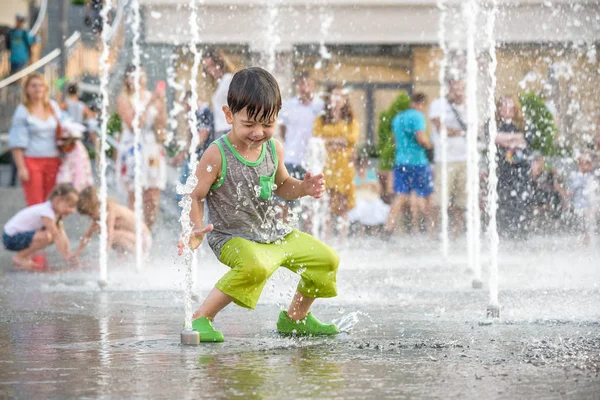 Heyecanlı çocuk su jetleri, Çeşme arasında eğleniyor. Şehirde yaz. Çocuk mutlu gülümseme yüzünü. Ekoloji kavramı.