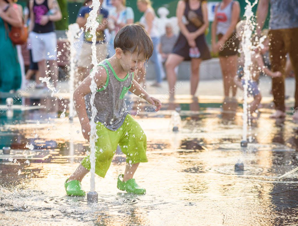 Excited boy having fun between water jets, in fountain. Summer in the city. Kid happy smile face. Ecology concept.