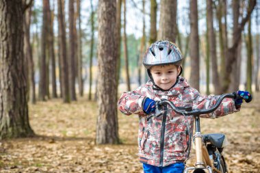 Güzel sonbahar gününde bir bisiklet ile sonbahar ormandaki eğleniyor 3 veya 5 yıllık mutlu bir çocukluk oğlan. Etkin alt giyen Bisiklet kask. Güvenlik, spor, eğlence çocuk kavramı ile