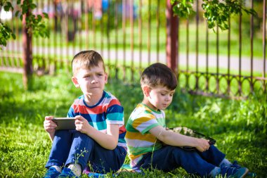 İki kardeş çocuk tablet ile çim üzerinde yalan söylüyor. Dijital tablet veya bir film izlerken ya da müzik açık havada için dinleme telefon ile oyun oynayan çocuk. Sağlıksız çocukluk kavramı