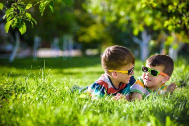 Mutlu gülümseyen erkek kardeş kardeşi çimenlerin üzerinde rahatlatıcı. Kopya alanı görünümüyle kapatın. Okul öncesi çocuklar güneş gözlüğü takıyor yaz tatil kampı. Gevşeme mutlu çocukluk dostluk kavramı.