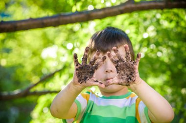 Çamur ve kumsalda oynadıktan sonra kirli ellerini gösteren beyaz bir çocuk. Güneşli bahar ya da yaz akşamları çiçek ağaçlarının arka planında. Mutlu çocukluk arkadaşlığı kavramı.