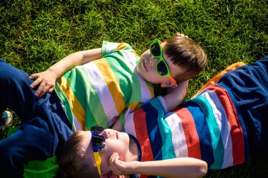 Mutlu gülümseyen çocuklar, çimenlere uzanmış, güneş gözlüğü takmış, kameraya gülümsüyor, yukarıdan çekim yapıyorlar. Mutlu çocukluk arkadaşlığı kavramı.