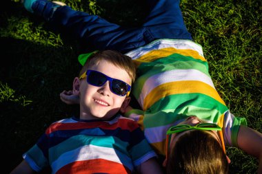 Mutlu gülümseyen çocuklar, çimenlere uzanmış, güneş gözlüğü takmış, kameraya gülümsüyor, yukarıdan çekim yapıyorlar. Mutlu çocukluk arkadaşlığı kavramı.