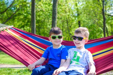 İki kardeş kardeş sıcak güneşli günde hamakta orman veya Şehir Parkı üzerinde rahatlatıcı güneş gözlüklü. Kardeşler birlikte eğleniyor çocuk evlat. Dostluk kavramı.
