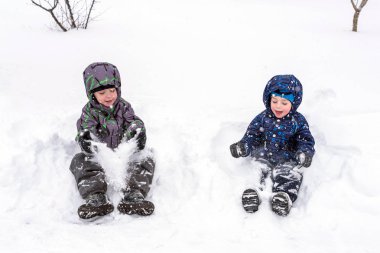 İki komik küçük çocuk çocuklar açık havada oynamak renkli giysiler içinde. Kışın soğuk karlı günlerde çocuklu etkin boş. Mutlu arkadaş kar ile eğleniyor
