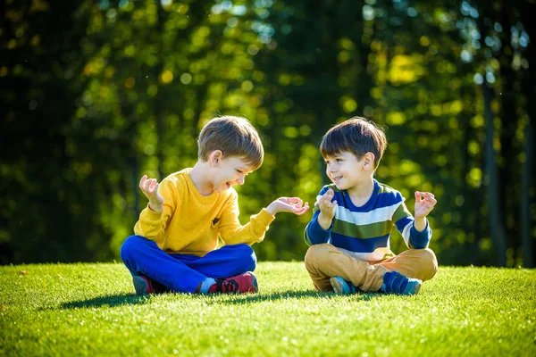 İki beyaz erkek kardeş taze yeşil çimen tarlasında oturuyor ve günlük giysiler içinde meditasyon yapıyor, mutlu çocuklar dışarıda huzurlu bir yaz haftasonunun tadını çıkarıyor. Arkadaşlık rahatlama konsepti.