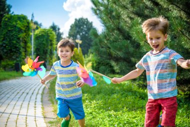 Yel değirmeni fırıldak ile bahçede oynayan iki mutlu çocuk. Çok güzel kardeş kardeş iyi arkadaş oldular. Güzel bir çocuk çocuk bahar ya da yaz park gülümse. Açık havada eğlence arkadaşlık aile kavramı.