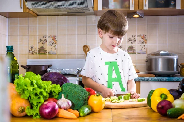 The young boy in cooking standing in the kitchen near table with vegetables. — Stock Image Young Boy Cooking Standing Kitchen Table Vegetables Royalty Free Stock Images