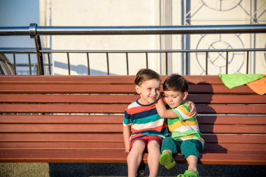 Şehirde yaz saati sıcak bir bankta oturan iki çocuk, erkek kardeşler, akşam, birbirlerine dostluk kavramı sarılma