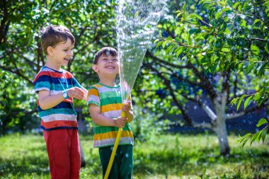 Mutlu çocuk çocuk bir hortum su dökülen. Çocuklar köyü açık havada bahçede meyve sulama ile eğleniyor. Komik tatil eğlence su çocuklar için.