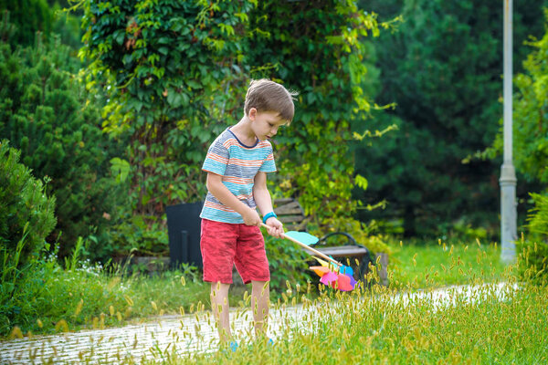 Portrait of a happy cute little boy holding pinwheel at the park. kid hold in hand play with windmill. boy smiling in spring or summer forest. Outdoors leisure weekend family concept.