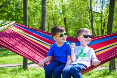 İki kardeş kardeş sıcak güneşli günde hamakta orman veya Şehir Parkı üzerinde rahatlatıcı güneş gözlüklü. Kardeşler birlikte eğleniyor çocuk evlat. Dostluk kavramı.