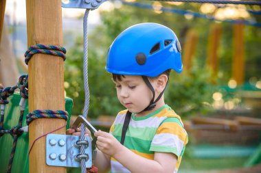 Küçük şirin çocuk aktivite bir tırmanma macera parkta yaz güneşli bir günde zevk. bir ip Bahçesi yapısında tırmanma yürümeye başlayan çocuk. Kask ve kemer ile güvenli tırmanma aşırı spor. sigorta