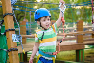 Küçük şirin çocuk aktivite bir tırmanma macera parkta yaz güneşli bir günde zevk. bir ip Bahçesi yapısında tırmanma yürümeye başlayan çocuk. Kask ve kemer ile güvenli tırmanma aşırı spor. sigorta