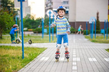 İki tekerlekli paten ve kardeş kardeşi parkta sarılmış scooter üzerinde çocuk evlat. Çocuk koruma vatkaları güvenli paten için binmek. Çocuklar için etkin açık spor.