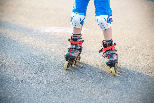 Little boy learning to roller skate in summer park. Children wearing protection pads for safe roller skating ride. Active outdoor sport for kids. Close up view of skates.