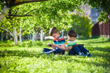 İki kardeş çocuk tablet ile çim üzerinde yalan söylüyor. Dijital tablet veya bir film izlerken ya da müzik açık havada için dinleme telefon ile oyun oynayan çocuk. Sağlıksız çocukluk kavramı