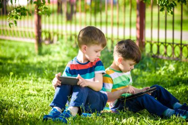 İki kardeş çocuk tablet ile çim üzerinde yalan söylüyor. Dijital tablet veya bir film izlerken ya da müzik açık havada için dinleme telefon ile oyun oynayan çocuk. Sağlıksız çocukluk kavramı