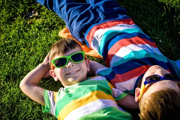 Mutlu gülümseyen çocuklar, çimenlere uzanmış, güneş gözlüğü takmış, kameraya gülümsüyor, yukarıdan çekim yapıyorlar. Mutlu çocukluk arkadaşlığı kavramı.