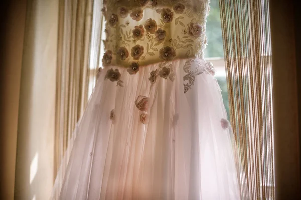 Elegantní růžové růže svatební šaty s vlakem visí na okně. — Stock fotografie